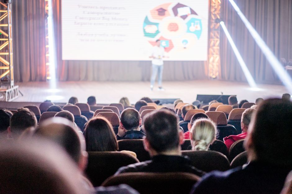 Mobilidade Urbana — Audience attentively watching a presentation in a conference setting, with stage lights and speaker