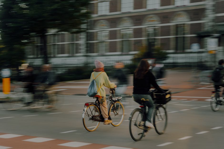 Mobilidade Urbana — Blurred cyclists riding through Amsterdam street at dusk, showcasing urban commuting culture in the