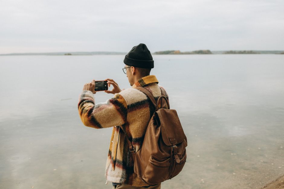 Mobilidade Urbana — Back view of a man capturing a lake with a smartphone, in a peaceful outdoor setting.