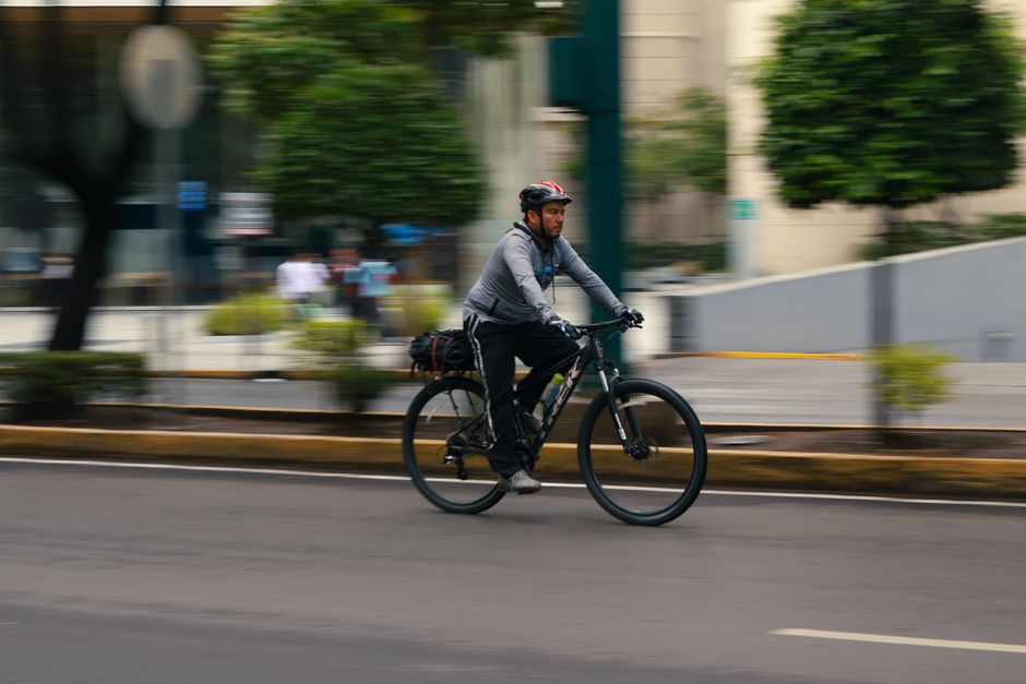 Mobilidade Urbana — A man cycling rapidly through city streets, showcasing urban biking in motion.